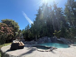 Zona de piscina con jacuzzi, sillas de descanso y vista a un área boscosa.