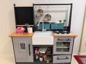 Una kitchenette con un lavabo, estufa, armarios de almacenamiento y un juego de cocina para niños.