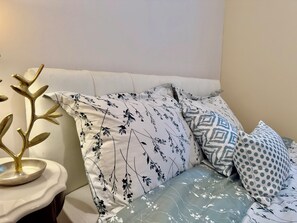 A bed with floral and geometric patterned pillows, a decorative gold plant, and a white bedside table. - hot tub villa with a sauna room (Surrey)