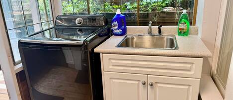 Una cocina funcional con lavadora, lavabo y ventana con vistas a la vegetación.