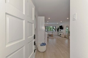 Un intérieur moderne avec une porte blanche, un coin salon comprenant un canapé et une table basse, ainsi qu’un grand miroir.