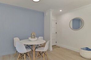 A dining area with a round table, white chairs, a white wall, and a blue accent wall. - Newly renovated 1-bed/bath condo sleeps 6! Walking distance to the beach! (Siesta Key)