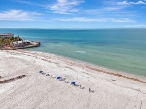 Ein Strand mit einer Reihe von Sonnenschirmen, einem Steg und einem Gebäude mit Blick auf den Ozean.