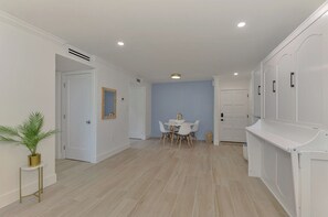 A modern interior with a dining area, white walls, and a light wooden floor. - Newly renovated 1-bed/bath condo sleeps 6! Walking distance to the beach! (Siesta Key)