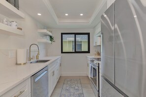 Eine moderne Küche mit weißen Schränken, einem Edelstahl-Kühlschrank, einem Einbauofen und einem Fenster über der Spüle.