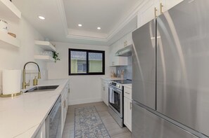 Een moderne keuken met witte kasten, roestvrijstalen apparatuur en een raam met jaloezieën.