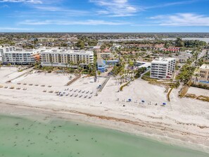 A beachfront hotel with multiple buildings, a sandy beach with umbrellas, and a clear view of the ocean. - Newly renovated 1-bed/bath condo sleeps 6! Walking distance to the beach! (Siesta Key)