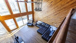 A high-ceilinged room with a wooden sloped ceiling, a black leather sofa, a leather armchair, and a chandelier. - Experience Stunning Scenic Views! (Knoxville)