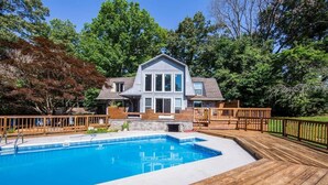 Una casa con piscina, terraza de madera y patio trasero cercado.