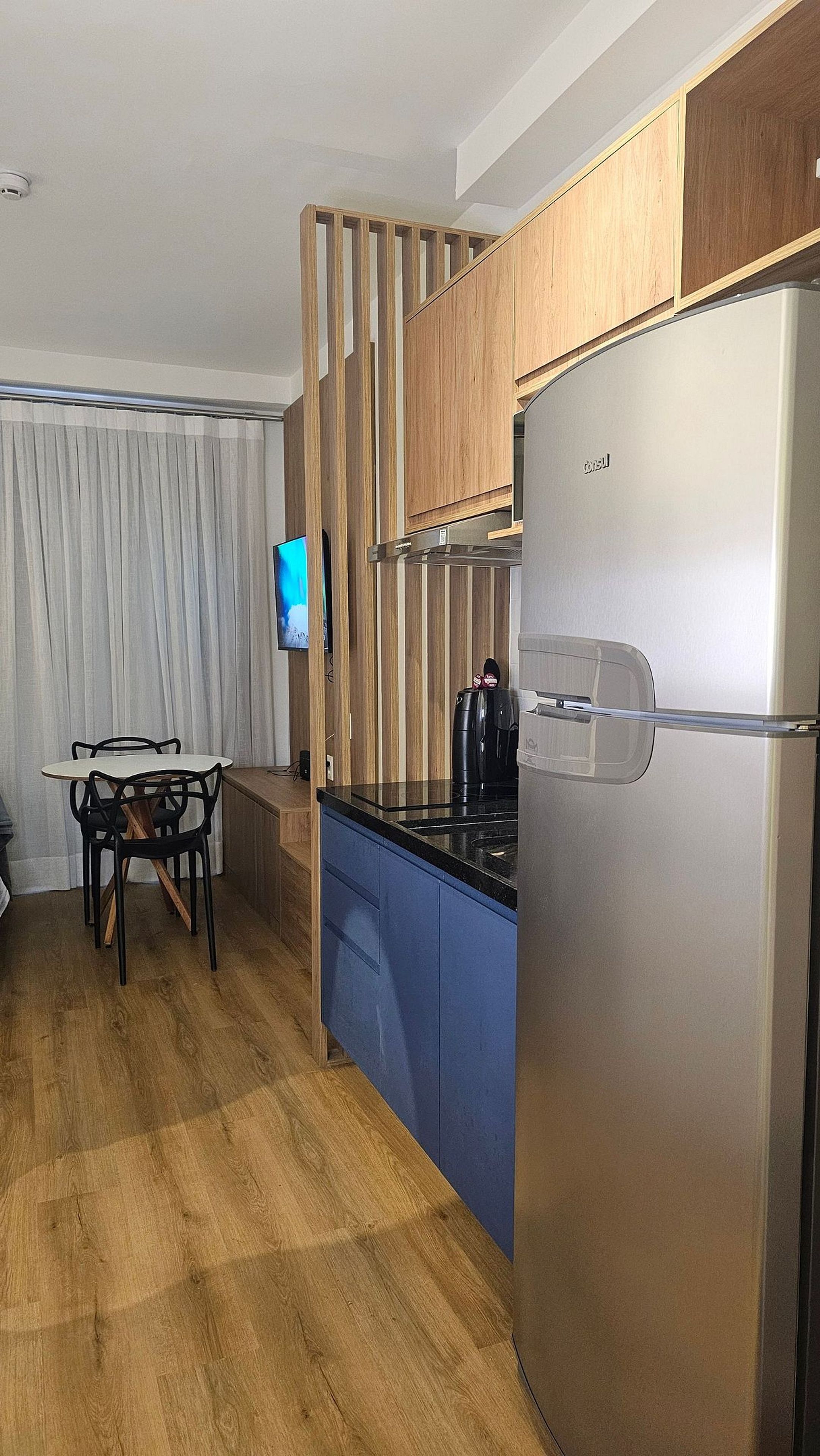 Cozinha moderna com geladeira de aço inoxidável, armários de madeira, bancada azul e área de jantar com mesa e cadeiras.