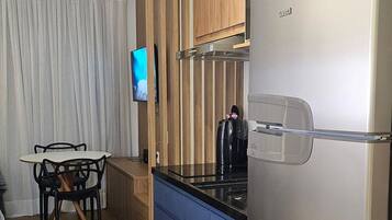 Cozinha moderna com geladeira de aço inoxidável, armários de madeira, bancada azul e área de jantar com mesa e cadeiras.