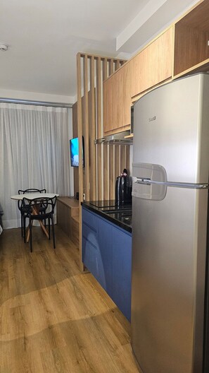 Cozinha moderna com geladeira de aço inoxidável, armários de madeira, bancada azul e área de jantar com mesa e cadeiras.