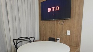 Una habitación con una mesa redonda, dos sillas, un televisor instalado en una pared de madera y un enchufe.