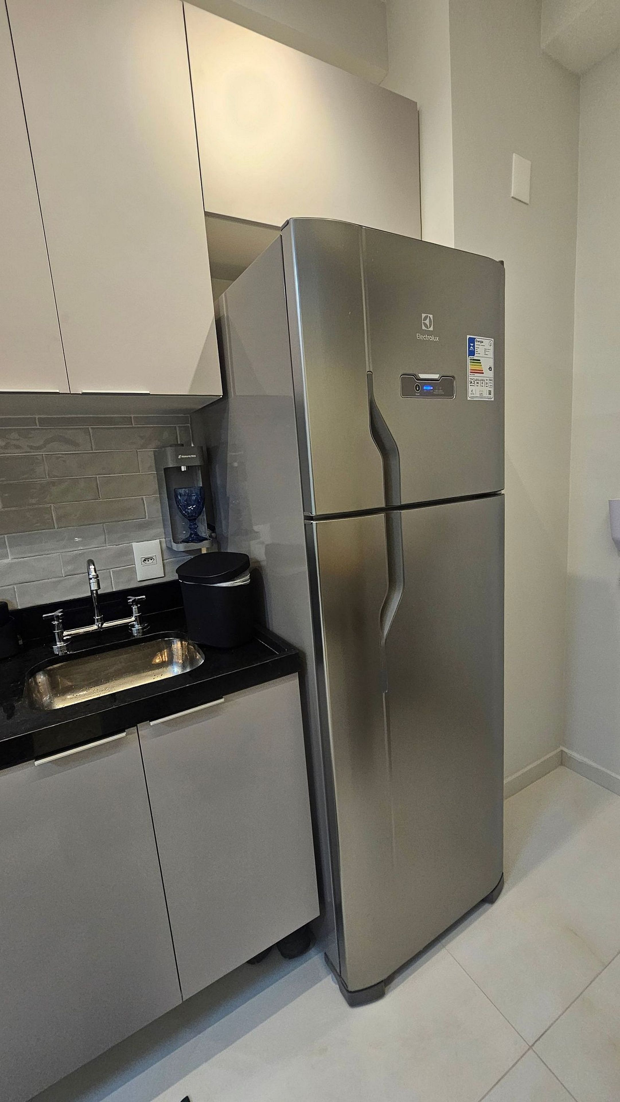 A stainless steel refrigerator in a kitchen with a tiled backsplash and a black countertop.