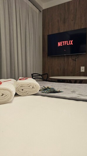 A hotel room with a bed, a TV displaying the Netflix logo, a table, and a chair. - Cond. Haus Mitre Reserva Vila Mariana  (São Paulo)