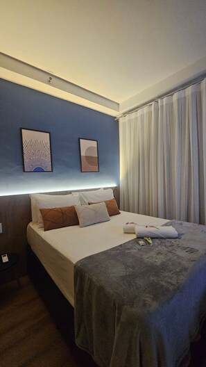 Habitació d'hotel amb un llit, una taula de nit i una finestra amb cortines.