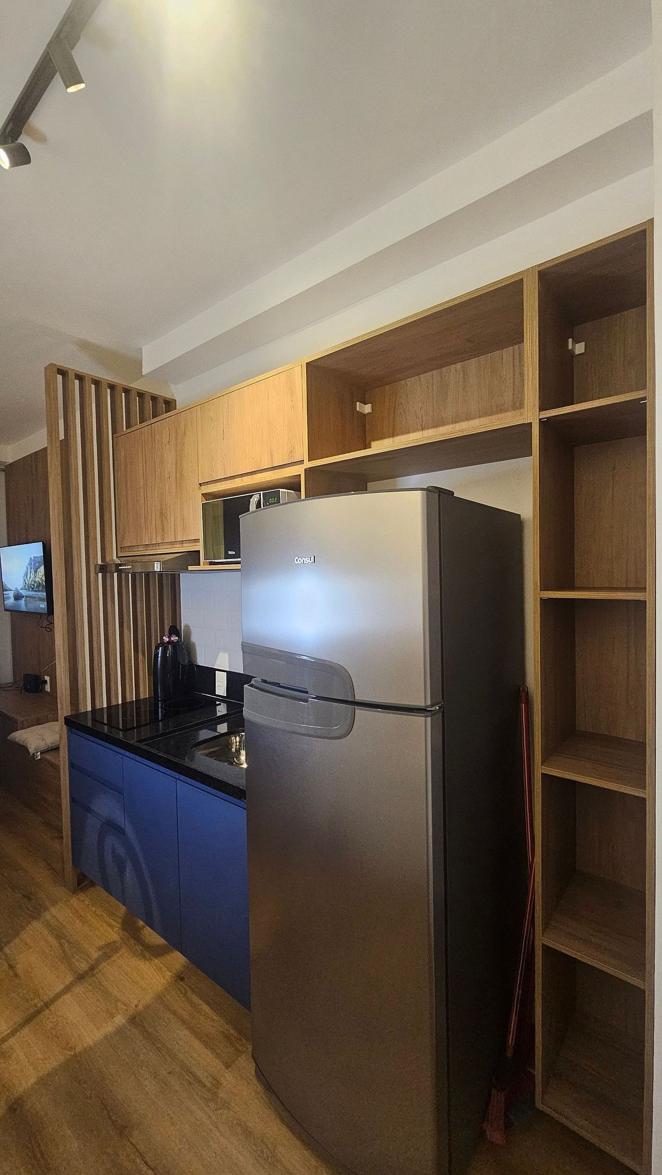 Una cocina moderna con refrigerador empotrado, armarios de madera y un televisor de pantalla plana montado en la pared.