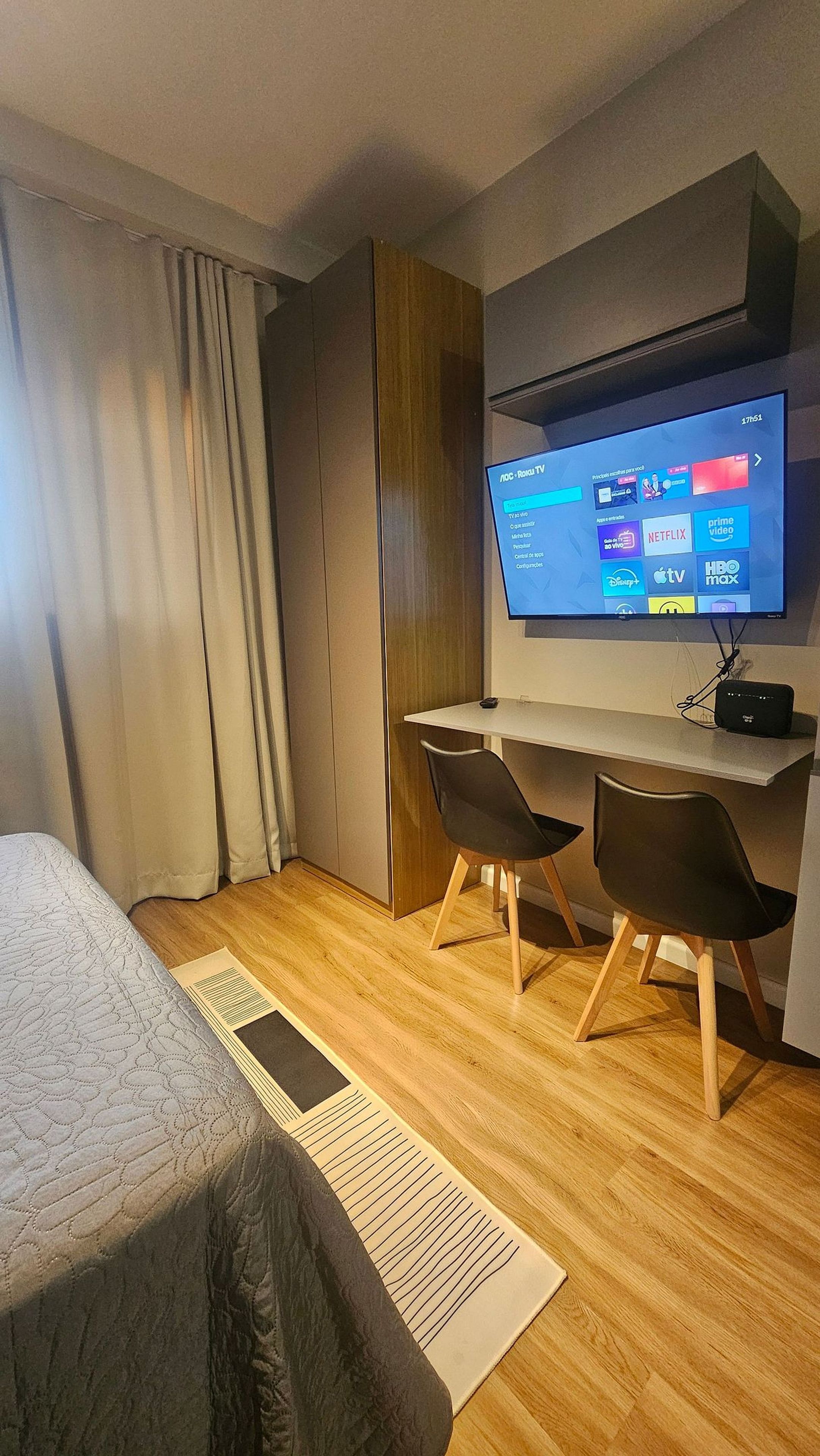 A hotel room with a bed, a desk, two chairs, a television, and a window with curtains.