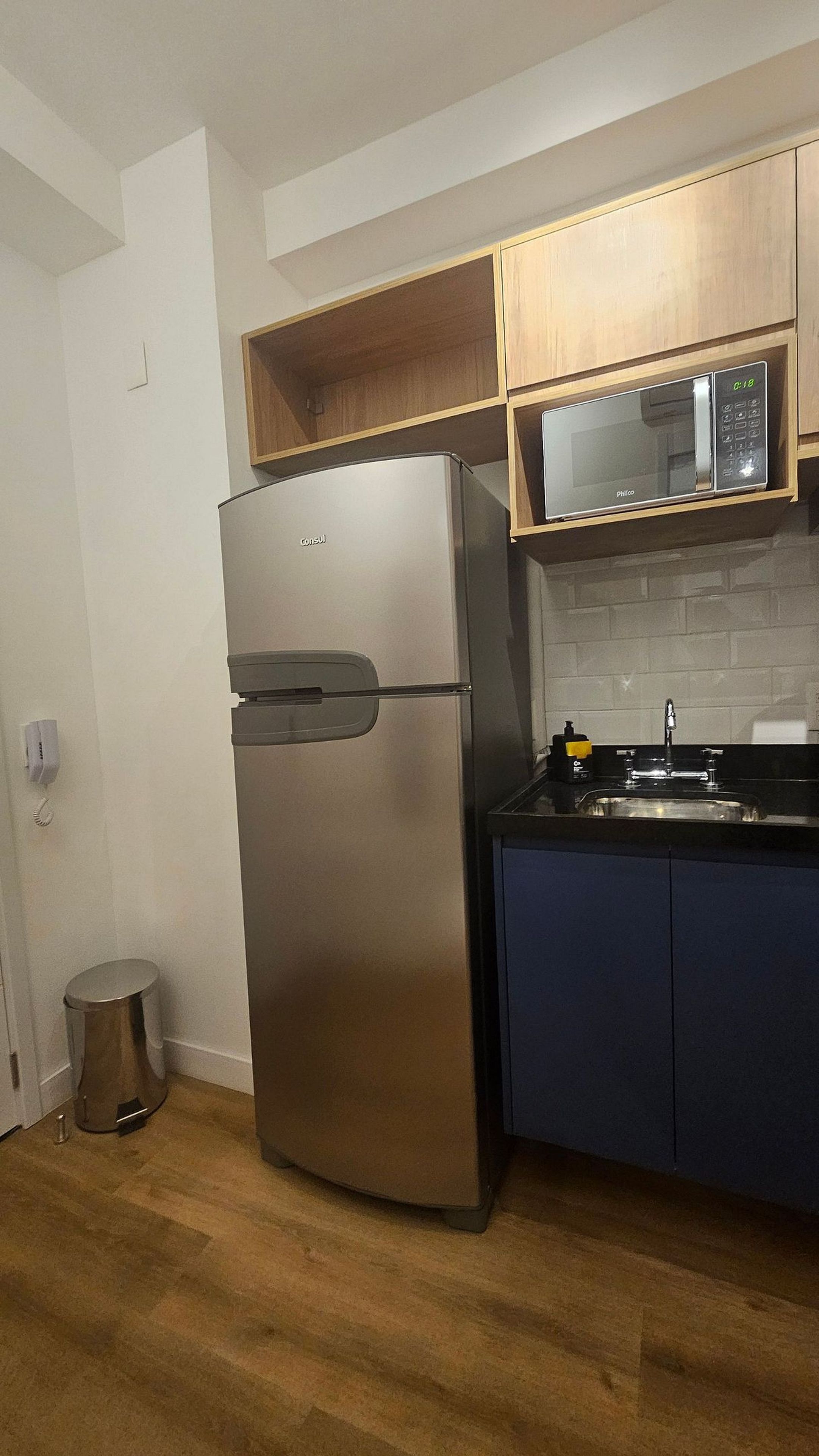 Uma cozinha compacta com geladeira de aço inoxidável, micro-ondas e pia.