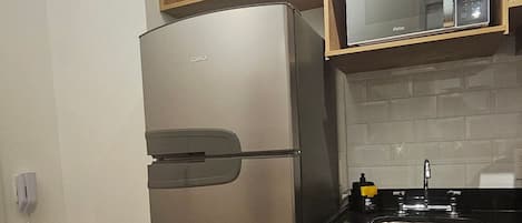 Une cuisine de taille réduite, équipée d’un réfrigérateur en acier inoxydable, d’un four à micro-ondes et d’un évier.