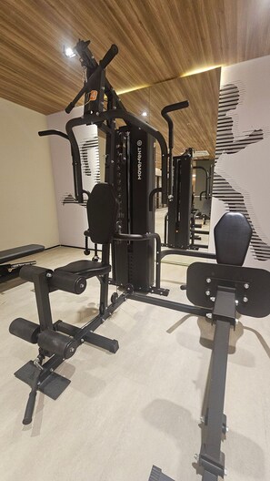 Un gimnàs amb diferent equipament per a exercicis, incloent una panca, màquines de peses i un mirall gran.