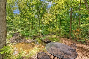 A forested area with a clear stream, a metal table, and a chair.
