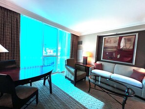 A hotel room with a balcony, a sofa, a table, and a lamp. - MGM Signature Deluxe Suite • Strip, Sphere & F1 Track Views • No Resort Fee (Las Vegas)