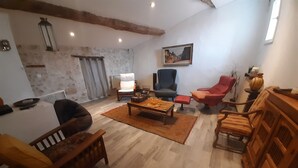 A living room with a wooden floor, a coffee table, a sofa, and a chair. There is a painting on the wall and a lamp on a side table. - Charming village house in the heart of the Luberon—a typical village house in the Luberon region (Grambois)