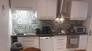 A modern kitchen with white cabinets, a coffee machine, a microwave, and a dining area with a glass table and chairs. - Charming village house in the heart of the Luberon—a typical village house in the Luberon region (Grambois)