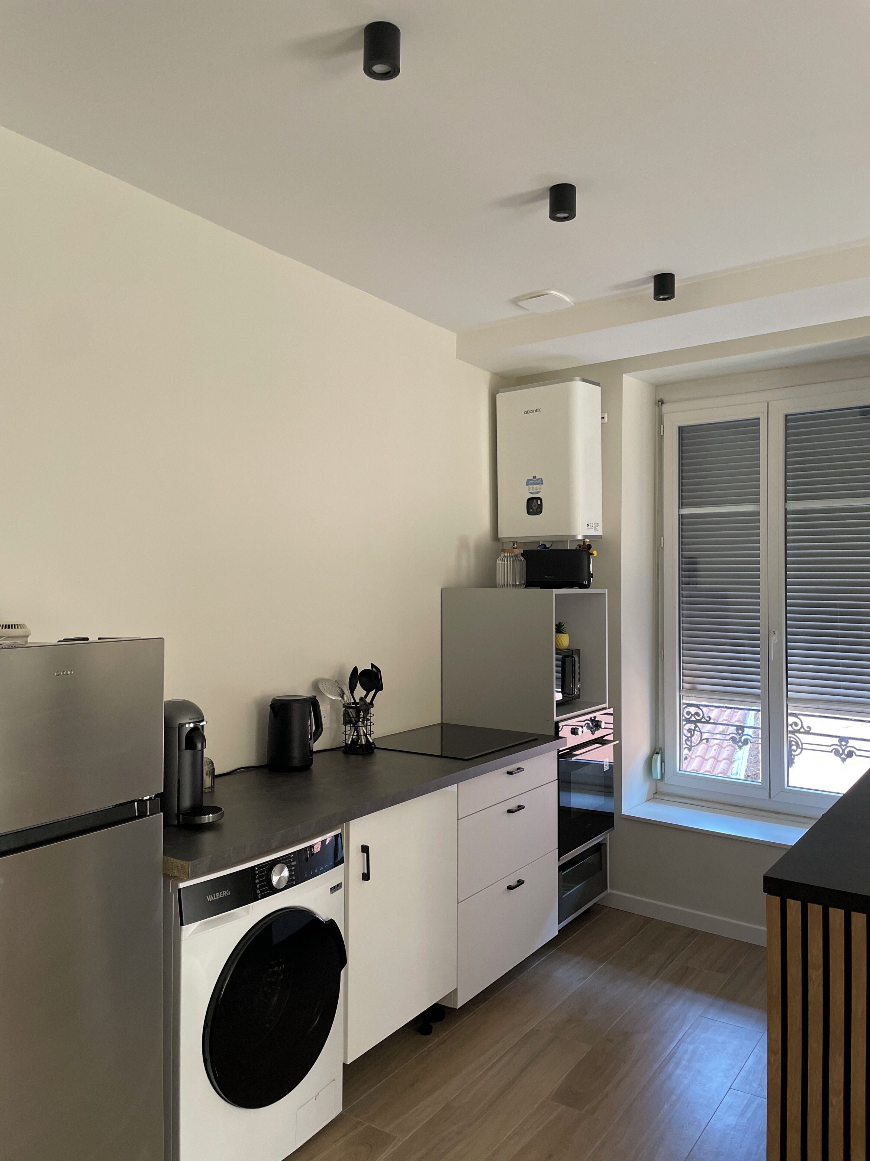 A compact kitchen with a washing machine, a coffee maker, and a water heater.