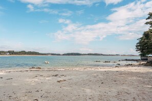 Ein Strand mit klarem Wasser, einem Boot und einer fernen Küstenlinie.