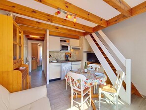 A cozy kitchen with wooden beams, a dining area with a floral tablecloth, and a staircase leading to an upper level. - Carnac - 3-room duplex apartment - 26m² (CARNAC)