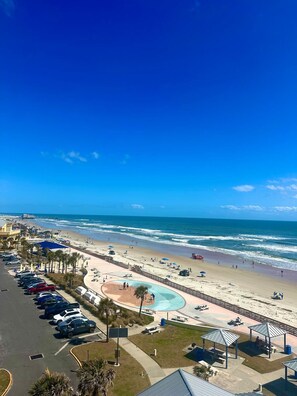 A beachside view with a parking lot, a swimming pool, and a beach area. - Oceanfront Studio, Beach & City Views, Jacuzzi, Heated Pool, Direct Beach Access (Daytona Beach)