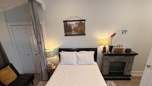 A bedroom with a bed, a nightstand, a lamp, a fireplace, and a door. - Cozy 1-bedroom private room in peaceful Daphne, minutes to Fairhope. (Daphne)