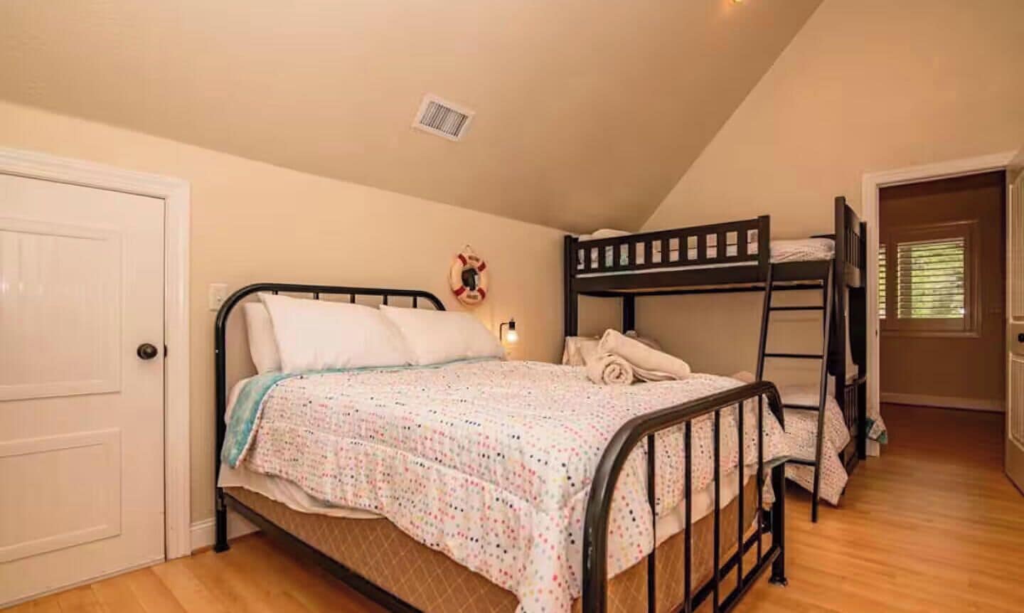 A bedroom with a bunk bed, a single bed, a door, and a wall-mounted light fixture.