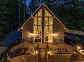 Une cabane en rondins dotée d’une grande fenêtre centrale, d’une véranda avec des balustrades et d’un mur en pierre.