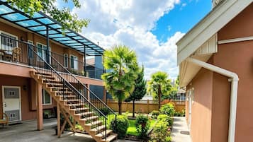 A residential building with a covered outdoor staircase, a palm tree, and a well-maintained garden.