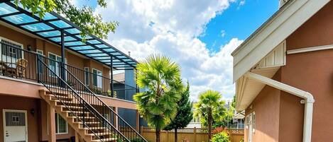 A residential building with a covered outdoor staircase, a palm tree, and a well-maintained garden.