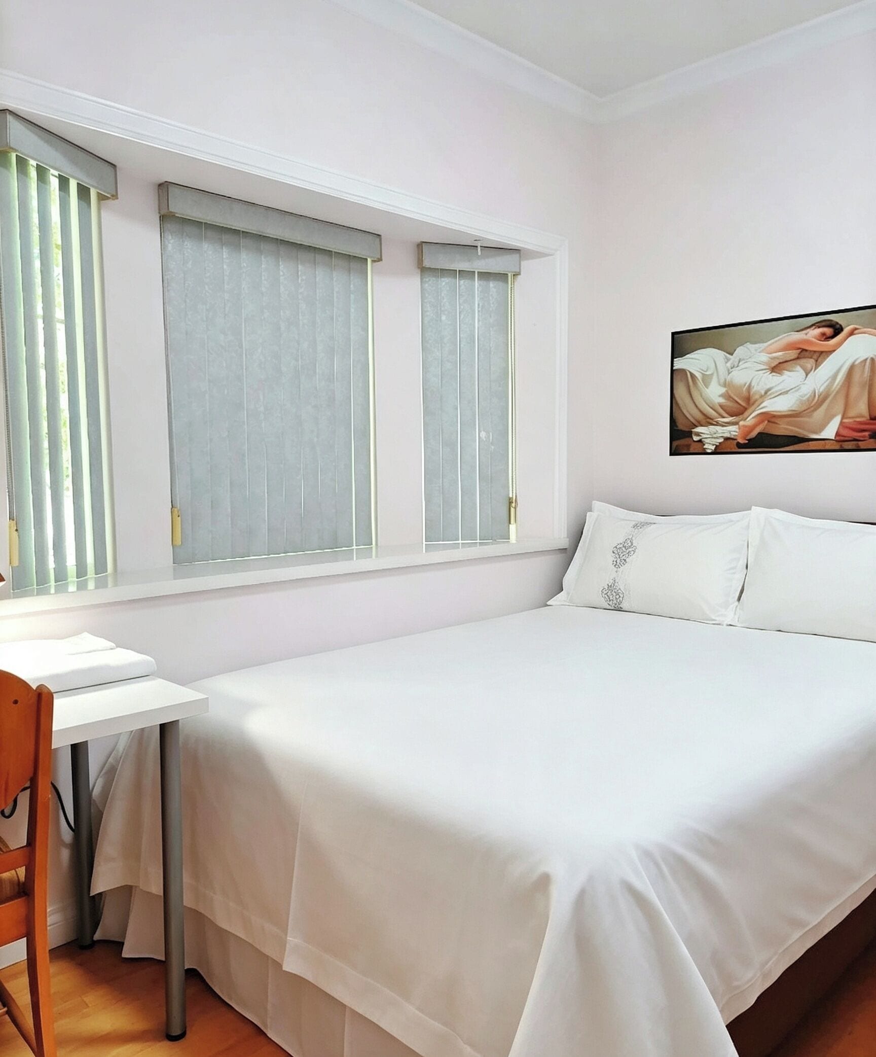 A bedroom with a bed, a desk, and a chair. There are two windows with curtains.