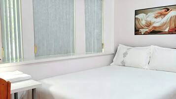 A bedroom with a bed, a desk, and a chair. There are two windows with curtains.