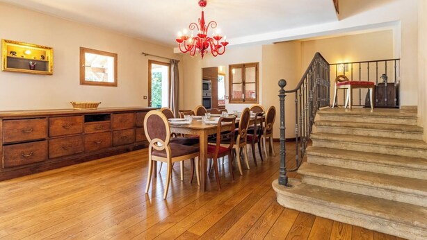 A spacious dining area with wooden flooring, a chandelier, and a staircase leading to an upper level. - La Ferme de la Galoppaz (THOIRY)
