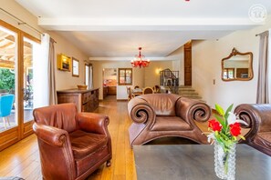 A spacious living room with leather armchairs, a dining area, and a kitchen in the background. - La Ferme de la Galoppaz (THOIRY)