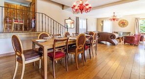 A dining area with a wooden table and chairs, a staircase, and a living room with a sofa and a red chair. - La Ferme de la Galoppaz (THOIRY)