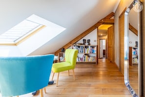 A room with a sloped ceiling, wooden flooring, a skylight, a blue chair, a green chair, and a bookshelf. - La Ferme de la Galoppaz (THOIRY)