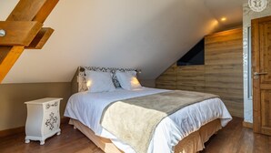 A bedroom with a sloped ceiling, a bed with white bedding, a wooden wardrobe, and a small bedside table. - La Ferme de la Galoppaz (THOIRY)