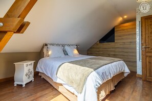 A bedroom with a sloped ceiling, a bed with white bedding, a wooden wardrobe, and a small bedside table. - La Ferme de la Galoppaz (THOIRY)