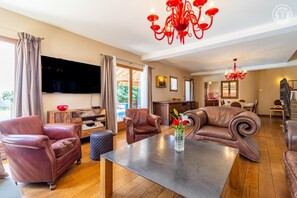 Ein geräumiges Wohnzimmer mit Ledersofas, einem Flachbildfernseher, einem Essbereich und einer Küche.