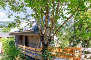 Ein traditionelles japanisches Haus mit einer Holzterrasse, umgeben von Grün und Blick auf einen Berg.