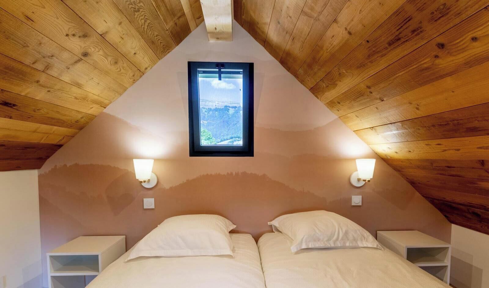 Ein Schlafzimmer mit zwei Betten, einer schrägen Decke, Holzwänden und einem Fenster.
