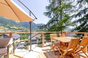 A wooden deck with a table and chairs, overlooking a mountainous landscape. - Chalet Under the Walnut Tree (SAINT JEAN D'ARVEY)